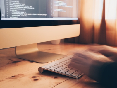 Image of a person typing on a keyboard in front of a computer screen.